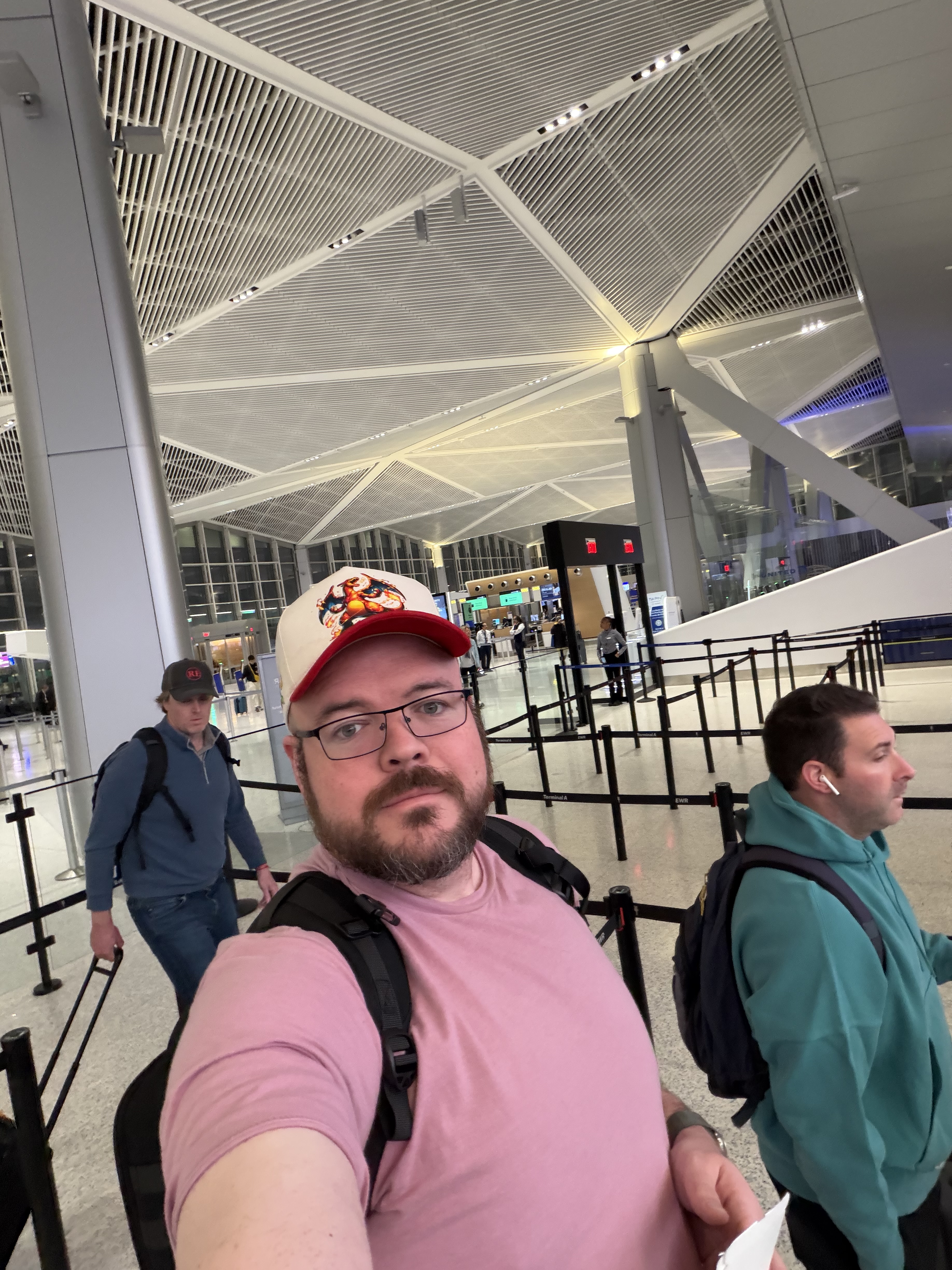 Sly Panorama at an airport terminal wearing a Charizard cap, backpack, and pink tee.