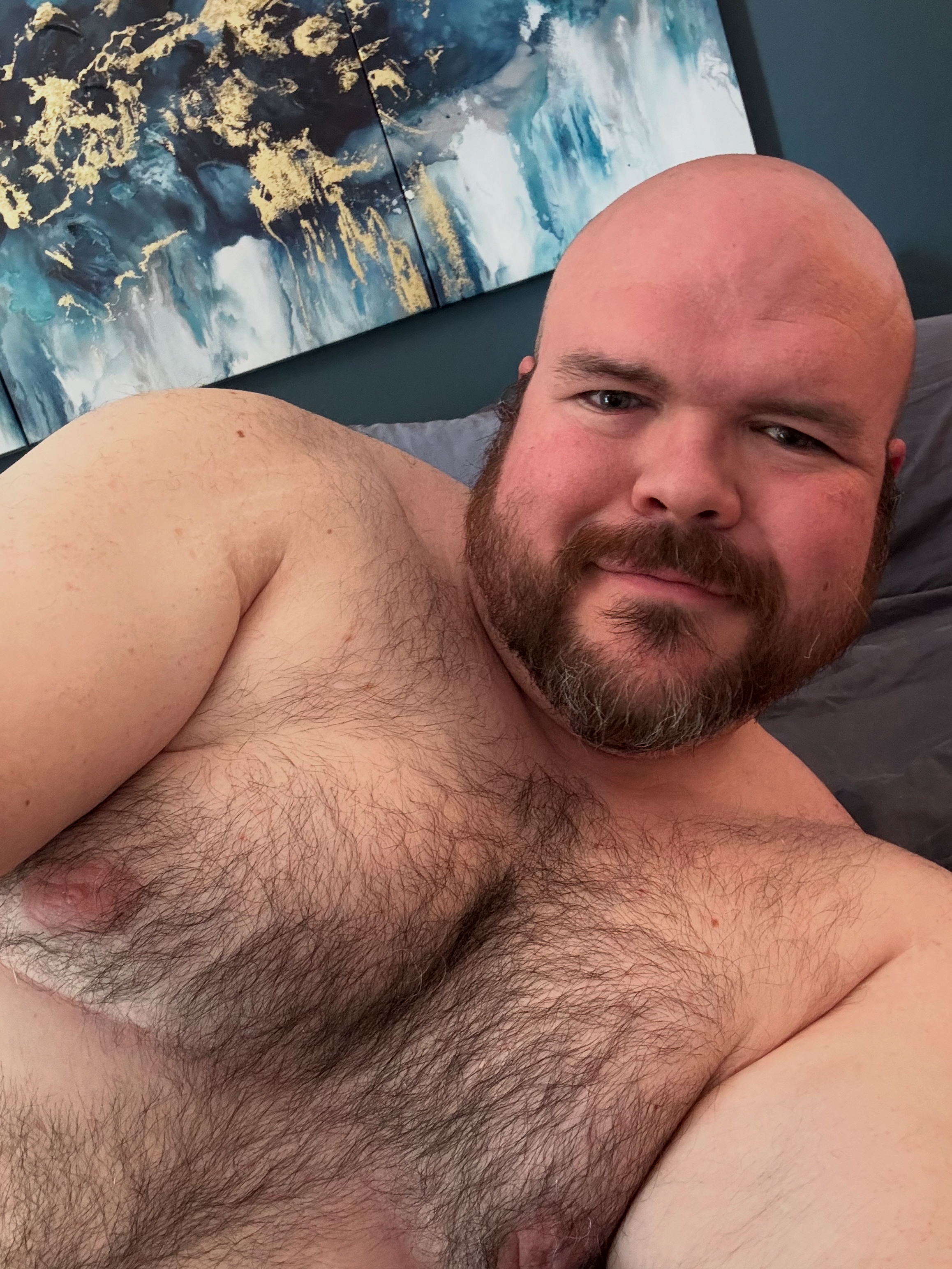 Sly Panorama shirtless and smiling with a large blue and gold triptych art piece behind him.